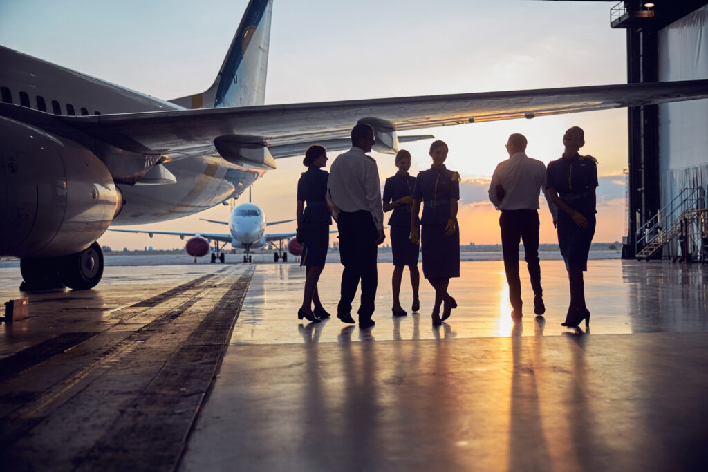 Arbeiten am Flughafen: Piloten und Flugbegleiter im Hangar vor einem Flugzeug bei Sonnenuntergang