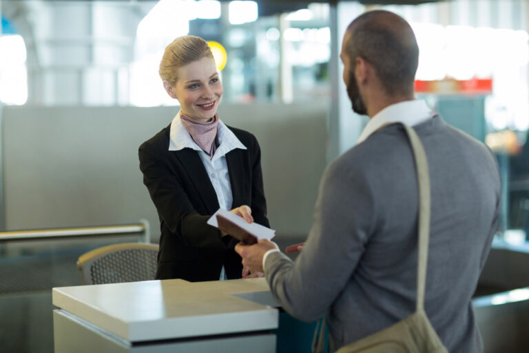 Servicekaufmann im Luftverkehr übergibt am Check-in eine Bordkarte
